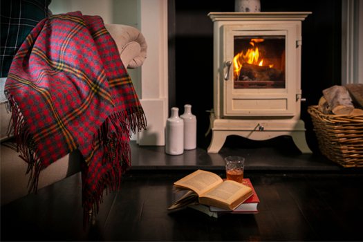 The Red Red Rose Lambswool tartan blanket on a sofa by a fireplace