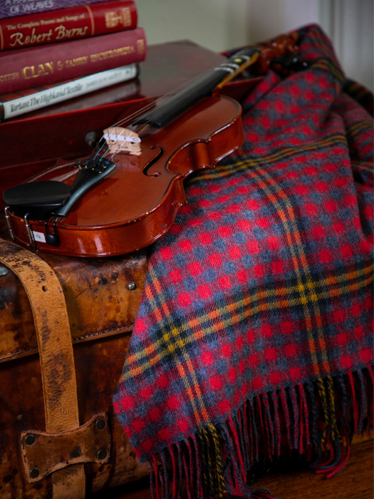 Tartan lambswool blanket beside a violin and a stack of Scottish books