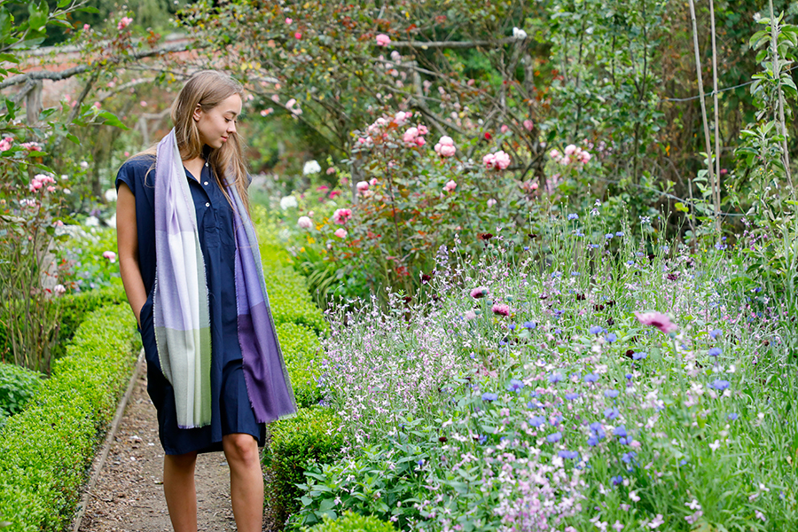 Model in flower garden wearing purple and green luxury scarf.