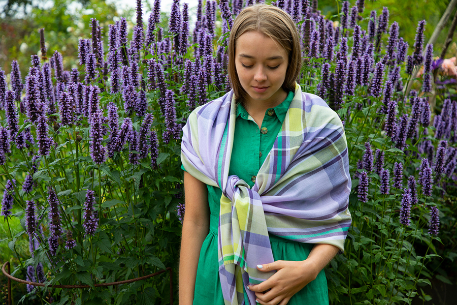 Model wears checked lilac and green scarf against floral background.